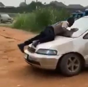 An FRSC Official clinging to the bonnet of a moving Honda car.